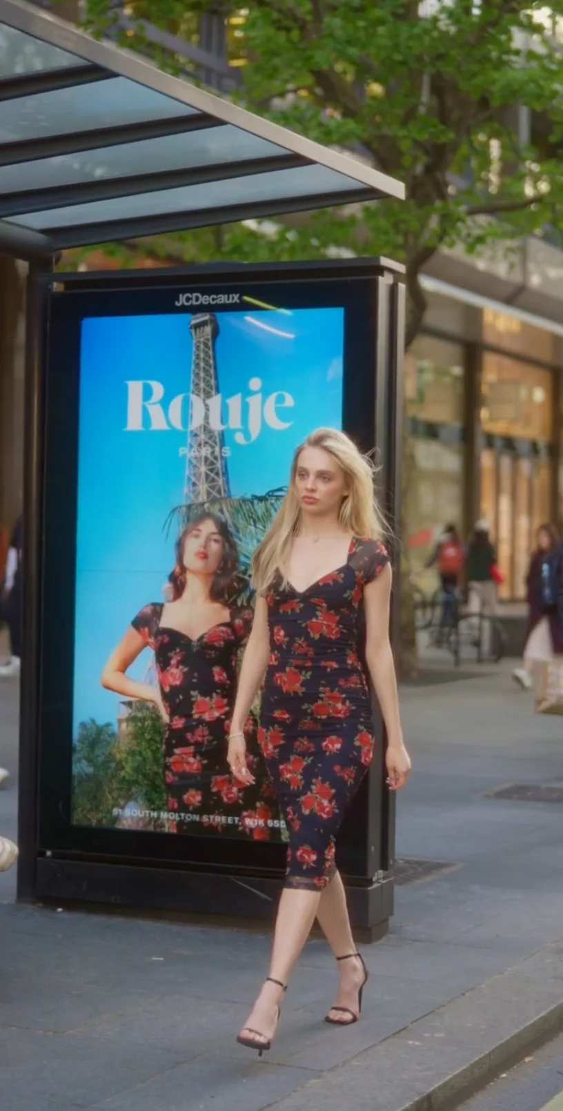 A model in a Rouje dress walking past the brand's campaign posters in London, filmed by We Stream